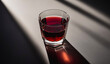 A glass filled with cherry liqueur casting a long shadow on a textured surface illuminated by sunlight