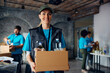 © Drazen - Happy female charity worker with donation box at food bank looking at camera.