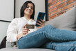 © O.Farion - Beautiful young woman lying on a couch, holding credit card and using mobile phone, smartphone for online shopping or internet payment