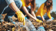 Focused volunteers in yellow wearing protective gloves pick up discarded plastic bottles, participating in an environmental cleanup effort outdoors