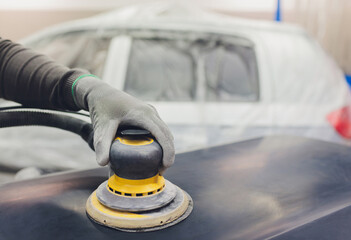 Auto mechanic preparing the car for paint job by applying polish with the power buffer machine