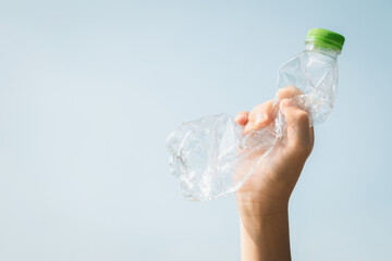  Recyclable plastic bottle held in hand up on sky background. Hand holding plastic waste for recycle reduce and reuse concept to promote clean environment with effective recycling management. Gyre