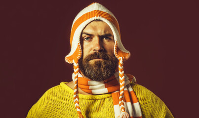 Wall Mural - Serious bearded man in yellow sweater, orange striped scarf and funny hat. Autumn-winter fashion. Casual look. Fashionable man in winter wear. Handsome man in woolen hat and scarf. Winter accessories.