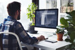 © Enigma - Man working on a computer in a home office setup with indoor plants and natural light.