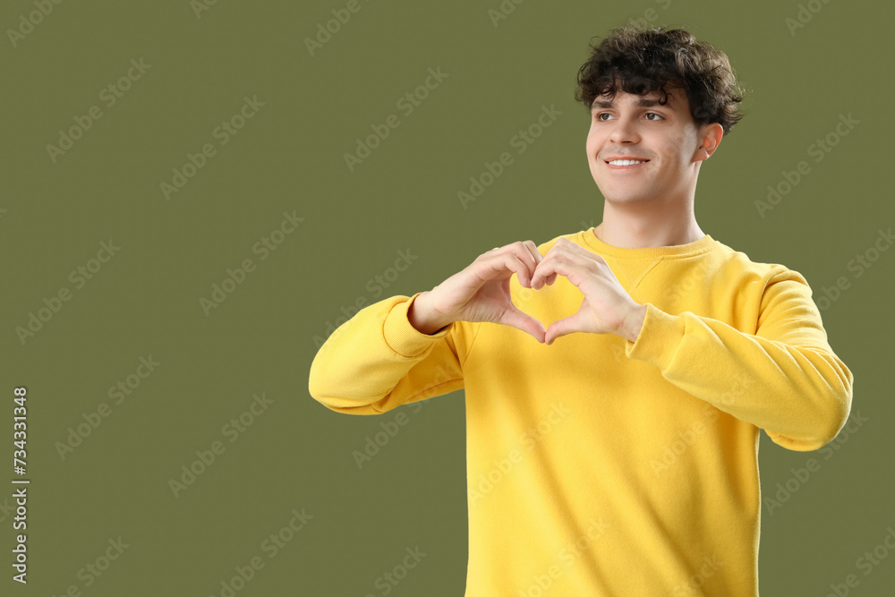 Handsome young man making heart with his hands on green background