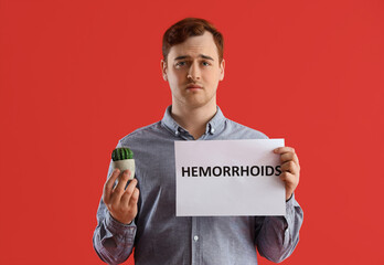 Sticker - Young man holding paper with word HEMORRHOIDS and cactus on red background