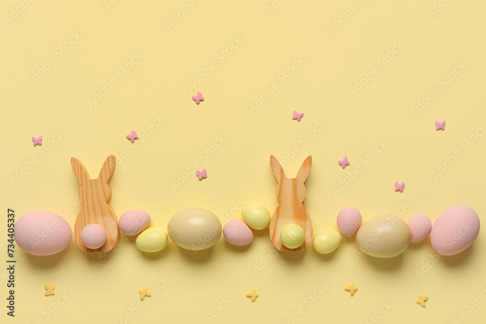 Composition with painted Easter eggs and wooden bunnies on beige background