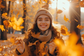 A joyful woman embraces the beauty of fall as she playfully tosses leaves in the air, her smiling face framed by a cozy hat and scarf