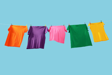 Sticker - Colorful t-shirts drying on washing line against light blue background, low angle view