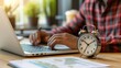 © JW Studio - Alarm clock on table in front of business man using laptop at home, concept of time management, work deadline.