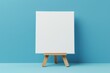 High quality photo of a white canvas mock up on a mini wooden tripod placed on a toy easel against a blue background