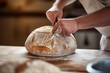 © altitudevisual - artisan baker scoring sourdough with a lame on a wooden countertop