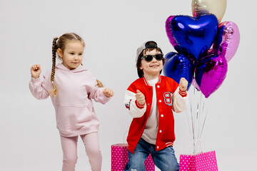 Happy children on a light background with bags after shopping or gifts at a children's party. Concept of shopping for children's clothing or gifts.