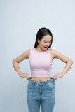 Fototapeta Sport - Successful weight loss, asian woman with too large jeans after effective diet, white background