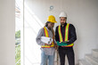 © chadchai - Two construction workers checking work schedule on tablet computer. Wear hardhat and safety vest, stand between stairway in construction site.