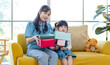 © Bangkok Click Studio - Happy mother's day Asian little cute girl child congratulating mom. Young mother and daughter smiling and holding gift on yellow cozy sofa in living room at home, Family holiday and togetherness.