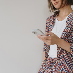 mobile phone in female hand. young pretty woman holds cell phone over white wall. social media, web 