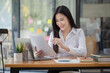 © SOMKID - Happy asian young businesswoman holding documents folders in office working space, Asian female employee using laptop talking on the phone at workplace.