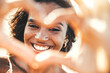 © Davide Angelini - Beautiful young woman making heart shape with hands - Happy black woman smiling at camera outdoors - Health care and self love concept