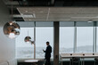 © Maskot - Rear view of businessman with smart phone standing by window at office