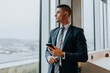 © Maskot - Thoughtful young businessman with smart phone looking out through window at office