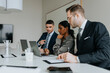 © Maskot - Business colleagues discussing strategy over laptop while sitting at conference table in board room