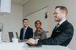 © Maskot - Smiling colleagues looking at businessman while sitting in board room