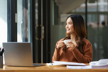 Fototapete - A young Asian businesswoman sitting and holding a white cup of coffee in the office.