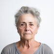 © Anna - An older woman with grey hair and a gray shirt stands in front of a neutral background.