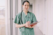 © Maskot - Portrait of confident female physician holding clipboard while standing in hospital corridor