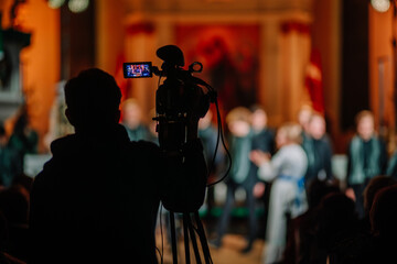 Valmiera, Latvia - January 7, 2024 - Saint Simon's Church. A cameraman recording a choir performance in a church, with the audience and performers in soft focus in the background.