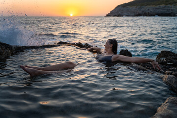 Young cheerful relaxed woman in a natural sea bath on the seashore. Thalassotherapy wellness concept