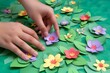 fingers placing paper flowers on a green paper lawn