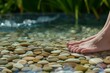 feet resting on pebbles in a shallow pool with a water stream