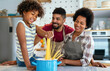 © NDABCREATIVITY - Happy african american family preparing healthy food in kitchen, having fun together on weekend
