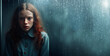 Young girl with red hair in blue shirt looking sadly through a rain-streaked window, evoking loneliness and contemplation.