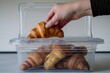 hand placing a croissant into a transparent lunchbox