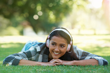 Wall Mural - Woman, headphones and streaming music on grass, radio and internet for podcast in outdoors. Female person, happy and relaxing on lawn, weekend playlist and subscription for audio or sound on vacation