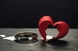 Symbolic representation of divorce featuring wedding rings, broken red heart on gray table with a paper cutout of a couple. Generative AI