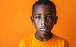 A multiracial young boy wearing a yellow shirt looks directly at the camera with a focused expression.