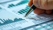 © Rattanathip - Close-up photo of a hand holding a pen and pointing to a bar graph, indicating detailed financial analysis and data review.