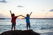© Anna - Silhouettes of two children, brothers. They stand with their backs holding hands against the backdrop of the sea at sunset. The concept of summer vacation, togetherness, friendship