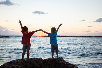 silhouettes of two children, brothers. they stand with their backs holding hands against the backdro