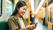 © colnihko - Young Asian woman is smiling and using her smartphone on a public bus