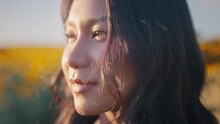 Closeup Face Of Asian Woman Opening Eyes On Sunset Background. Young Female Looking Straight At The Sunflower Field Landscape.