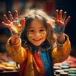 the little girl shows her hands with a palette of colors on her fingers and face