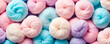 A close-up of many fluffy swirls of cotton candy, showing a variety of soft pastel tones that evoke a feeling of sweetness.