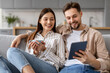 © Prostock-studio - Smiling european couple with coffee and tablet on the sofa