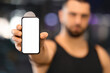 © Prostock-studio - Sports App. Serious muscular man holding blank smartphone in hand