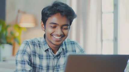 Wall Mural - Smiling indian business man working on laptop at home office. Young indian student or remote teacher using computer remote studying, virtual training, watching online education webinar at home office